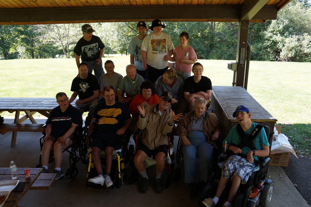 A large group of individuals and staff gathered under a picnic pavilion on a sunny day