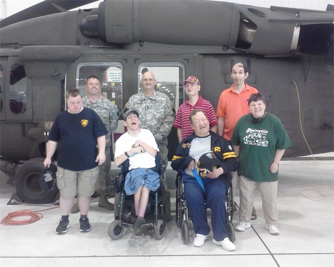 An Adult Training Facility group on a community tour, gathered with National Guard members in front of a helicopter
